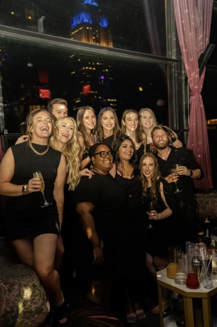 Friends with drinks at Suave Saturdays, the Empire State Building lit up behind them