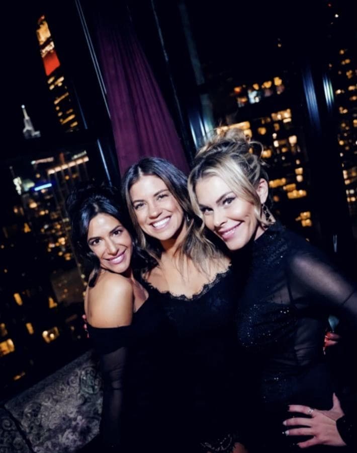 Three friends posing together with city lights behind them