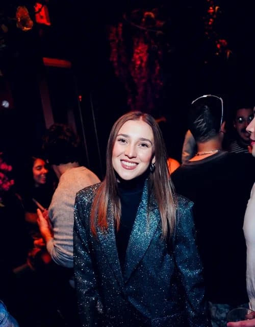 Woman in a sparkly black jacket smiling at the camera, enjoying the lively Suave Saturdays rooftop event in Manhattan.