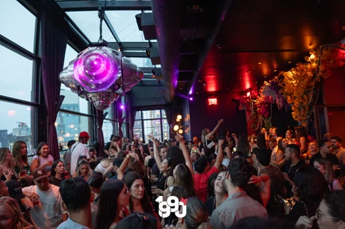 Packed dance floor at Suave Saturdays rooftop party, with a large purple disco ball hanging from the ceiling and a vibrant crowd.
