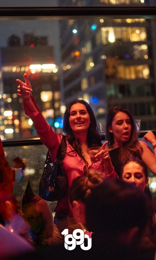 Woman in a red blouse raising her hand and smiling, enjoying the lively rooftop atmosphere at Suave Saturdays.