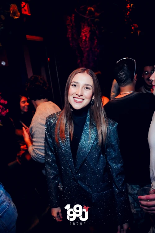 Woman in a sparkly black jacket smiling at the camera, enjoying the lively Suave Saturdays rooftop event in Manhattan.